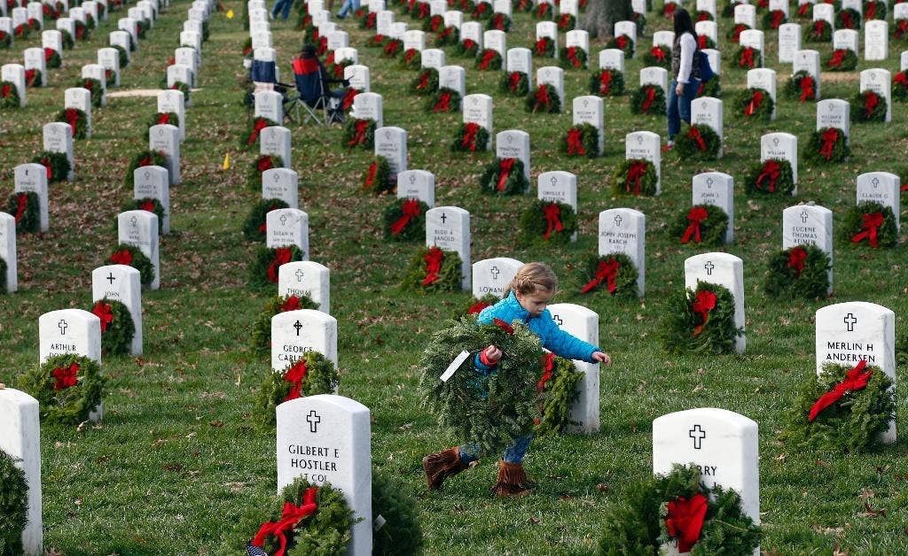 A child carries a wreath to a grave during Wreaths Across America at Arlington National Cemetery, Saturday, Dec. 12, 2015, in Arlington. (The Associated Press)