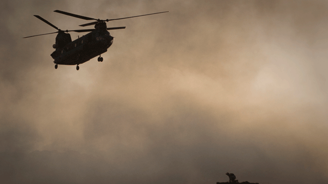 A US Marine tries to take cover, perched on a container, trying to shelter from the dust as a Chinook helicopter arrives to pick up supplies at Forward Operating Base Edi in the Helmand Province of southern Afghanistan, in this June 9, 2011 file photo.