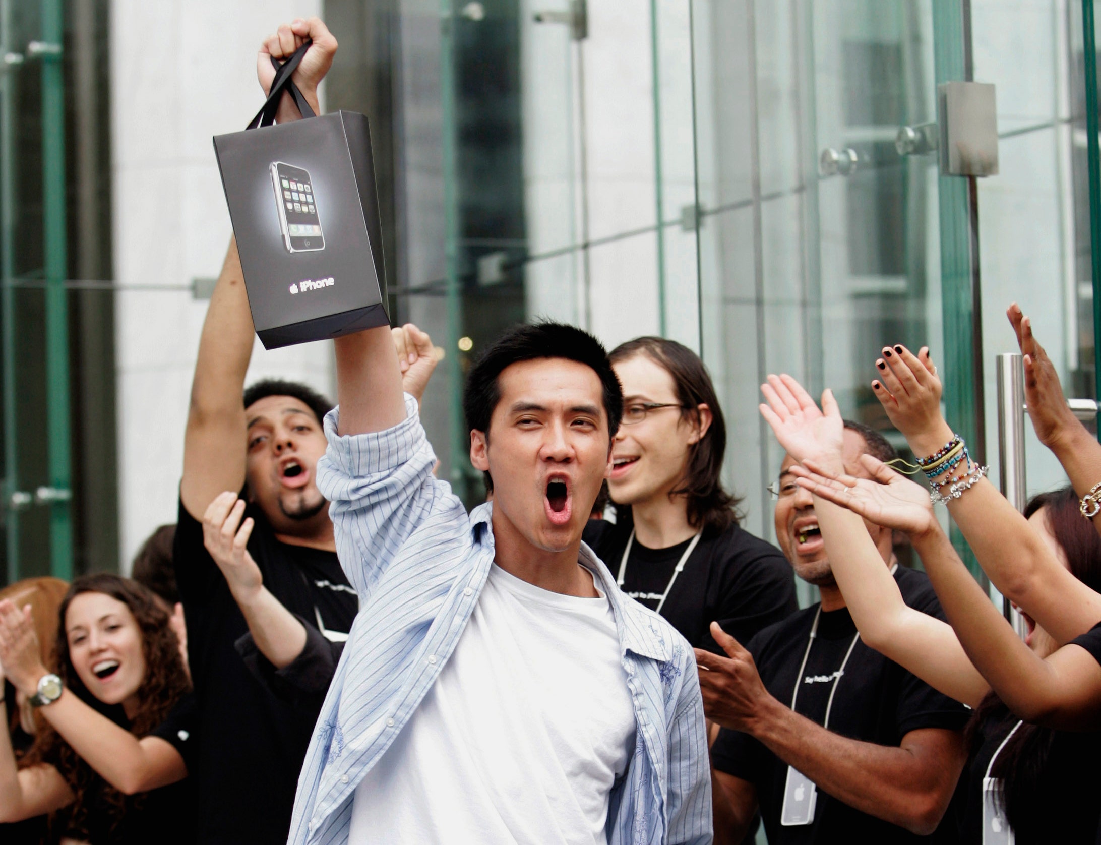 Surrounded by cheering Apple Store employees, one of the first iPhone buyers leaves the store on Fifth Avenue in New York, June 29, 2007. REUTERS/Jeff Zelevansky (UNITED STATES) BEST QUALITY AVAILABLE - RTR1RAZ0