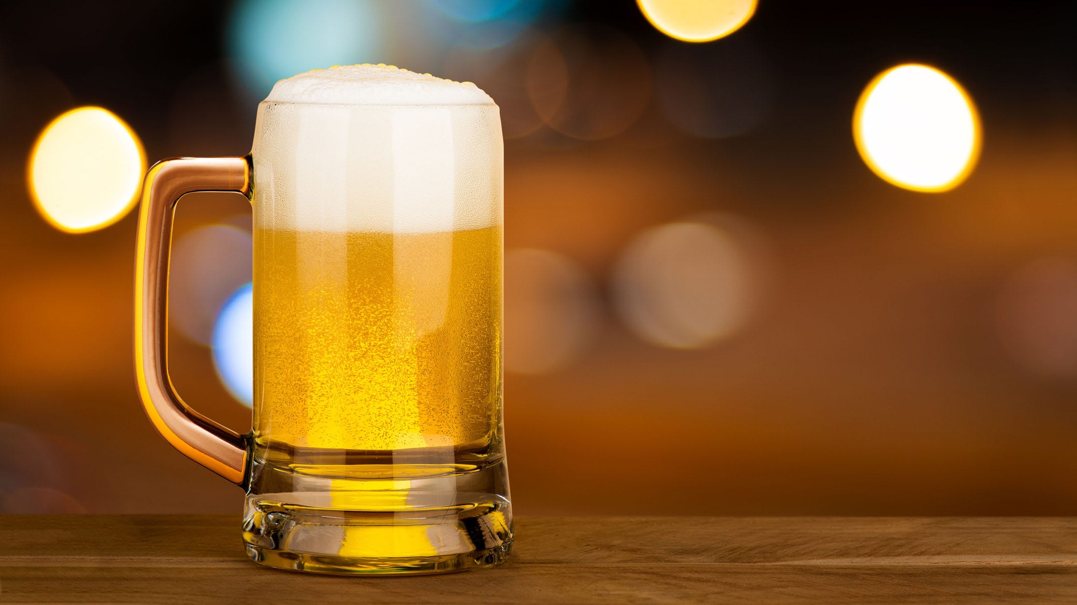 Segelas bir di atas meja kayu di pub dengan latar belakang malam cahaya bokeh, desain konsep perayaan minum alkohol dengan ruang fotokopi