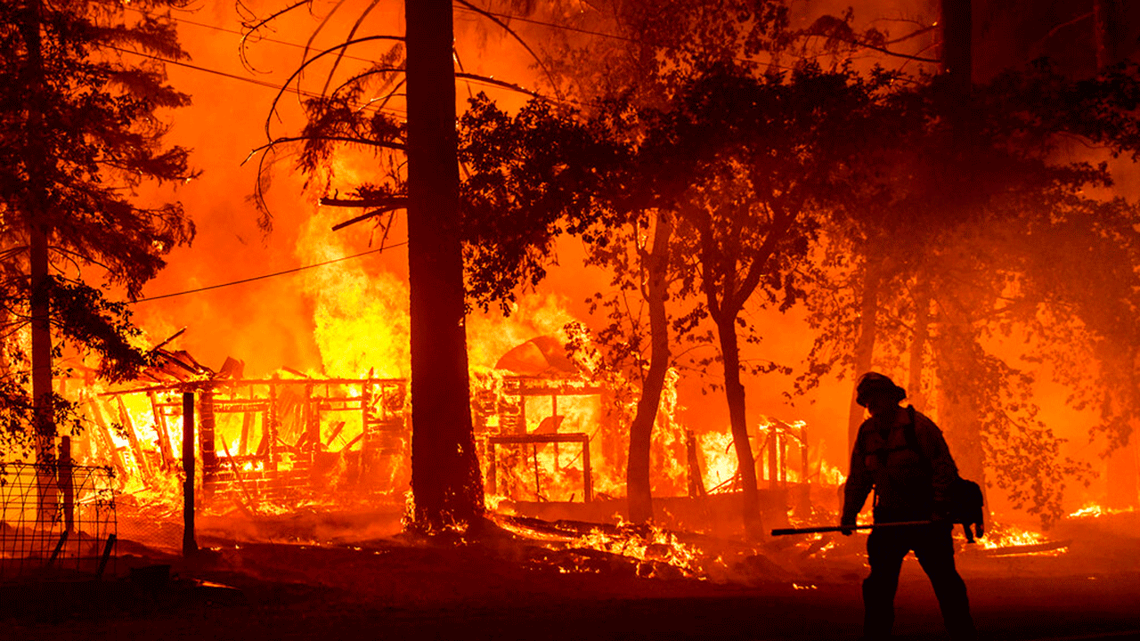 In this Saturday, July 24, 2021, file photo a firefighter passes a burning home as the Dixie Fire flares in Plumas County, Calif. The fire destroyed multiple residences as it tore through the Indian Falls community.