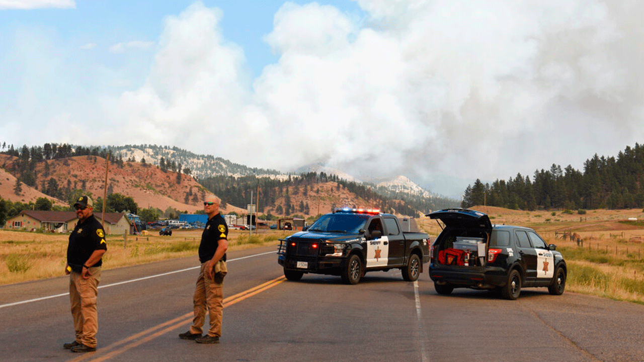 A plume of smoke rises from a wildfire as Cascade County sheriff's deputies prevent traffic from passing through along Highway 212 on Wednesday, Aug. 11, 2021, near Lame Deer, Mont. The Richard Spring Fire was spreading rapidly Wednesday as strong winds pushed it through rough, forested terrain. 