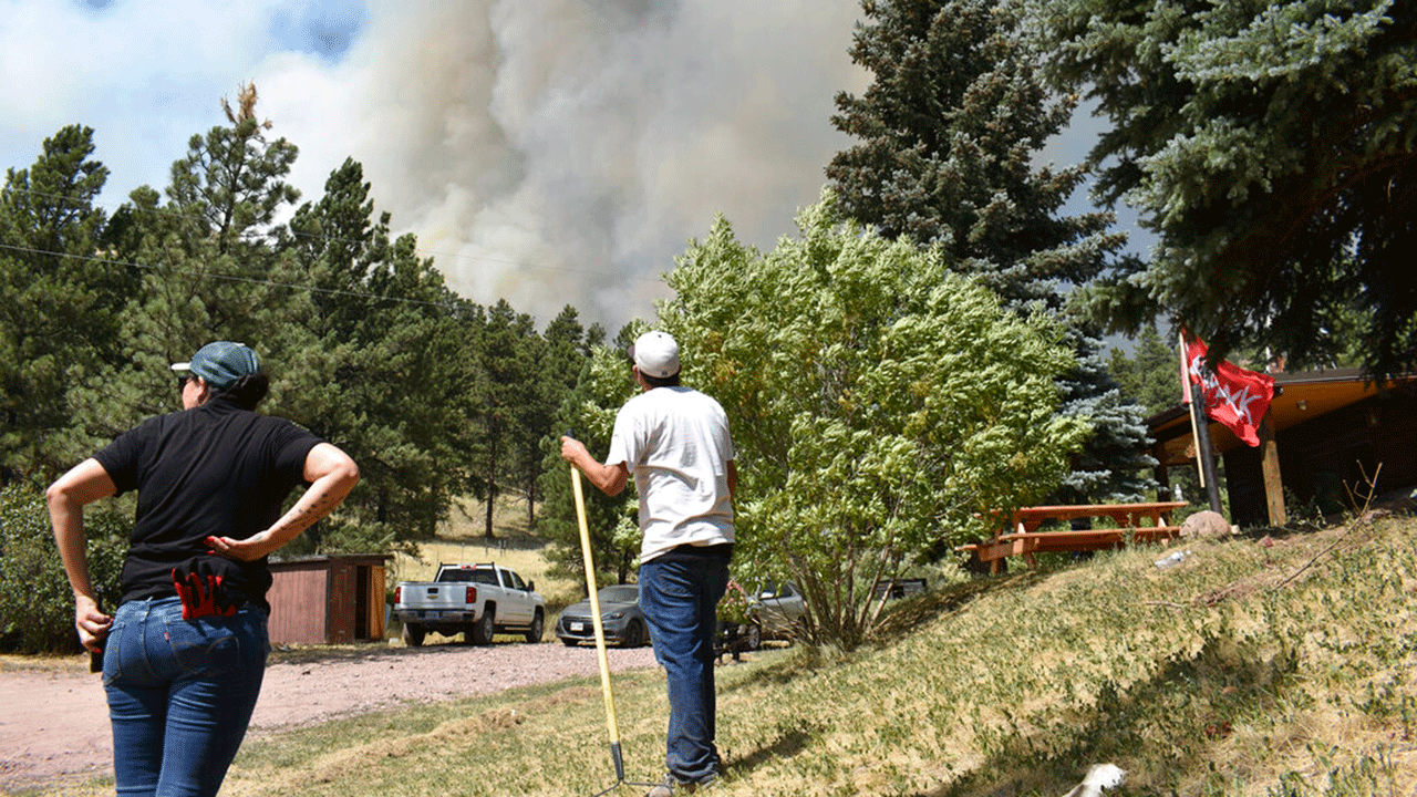 Krystal Two Bulls, left, and an unidentified friend watch smoke rise from the ridge top behind Two Bulls' house on the Northern Cheyenne Indian Reservation east of Lame Deer, Mont., Wednesday, Aug. 11, 2021. Two Bulls said that she's been preparing for the fire for two days by clearing brush around her house and packing her belongings in case she has to suddenly leave. The fire spread quickly Wednesday as strong winds pushed the flames across rough, forested terrain. In southeastern Montana, communities in and around the Northern Cheyenne Indian Reservation were ordered to evacuate as the Richard Spring Fire grew amid erratic winds. 
