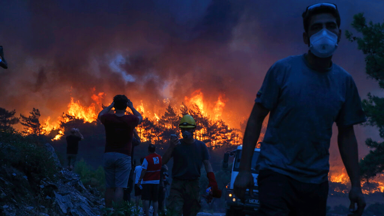 People watch a forest fire near the village of Akcayaka in Milas, Mugla in southwestern Turkey on Thursday, August 5, 2021. A forest fire that reached the compound of a coal-fired power plant in southwestern Turkey and forced evacuations by boats and cars, was contained on Thursday, after raging for about 11 hours, officials and media said.