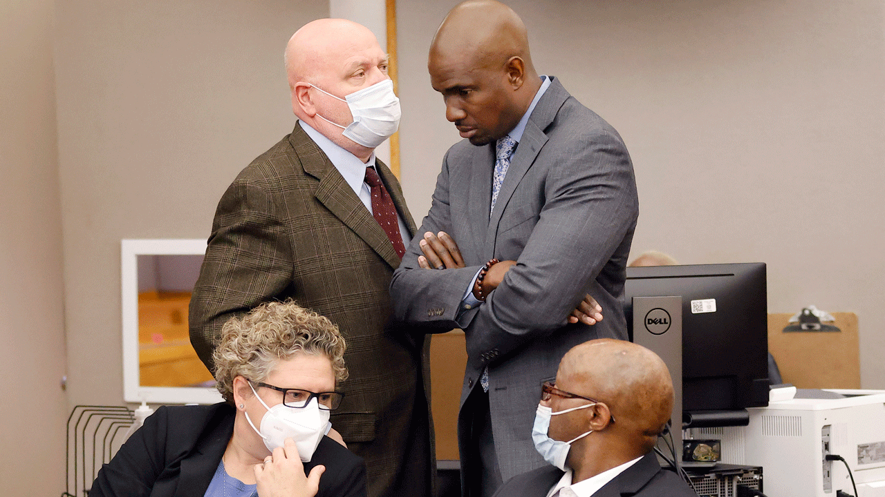 Defense attorney Kobby Warren, standing, right, listens to attorney Mark Watson, top left, as his client Billy Chemirmir, seated right, waits for motions and language being sent to the jury in his capital murder trial at the Frank Crowley Courts Building in Dallas, Friday, Nov. 19, 2021. He was joined by private investigator Tonia Silva seated, left. Chemirmir, 48, faces life in prison without parole if convicted of capital murder for smothering Lu Thi Harris, 81, and stealing her jewelry. He is accused of killing at least 18 women in Dallas and Collin counties. (Tom Fox/The Dallas Morning News via AP, Pool)