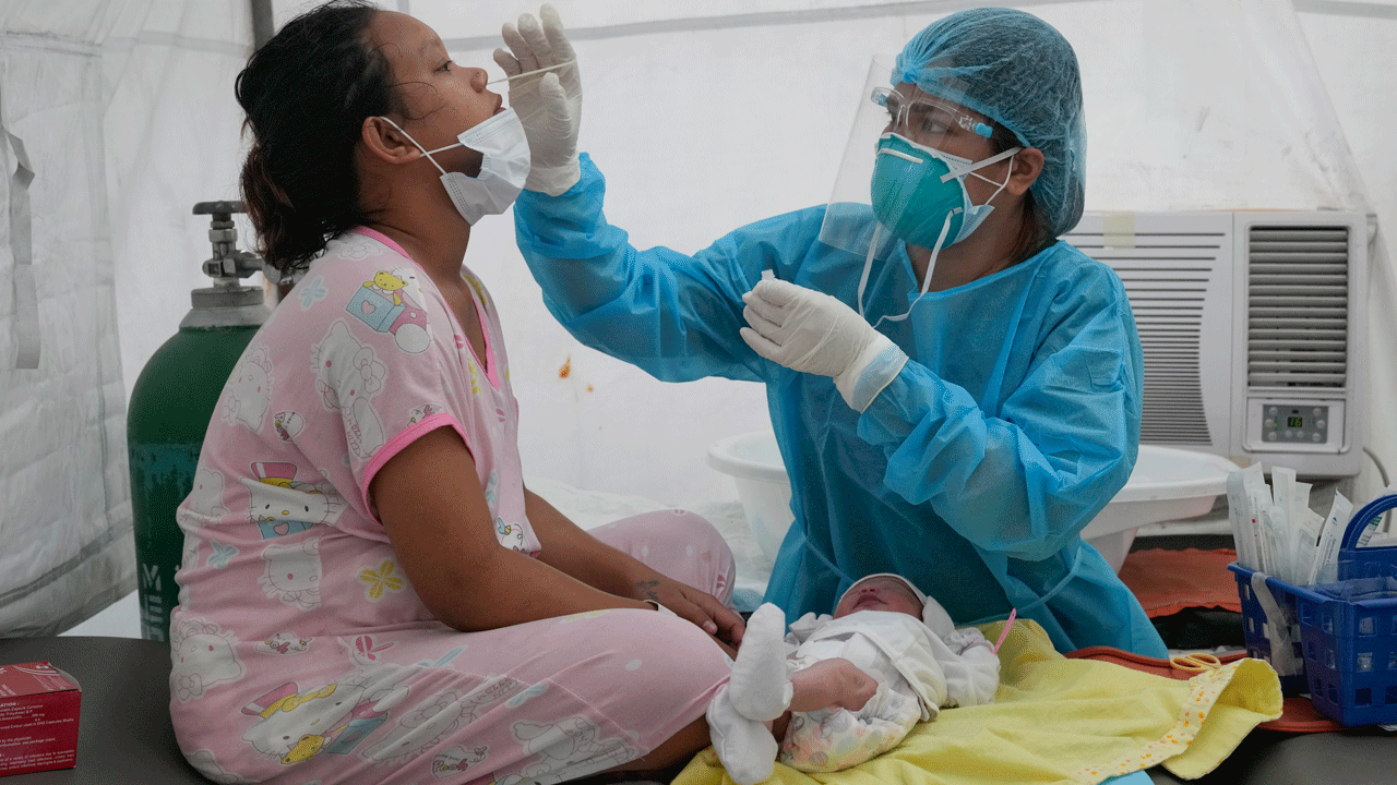 Medical Technologist Erika Alvarado performs a COVID-19 test on a patient who just delivered a baby outside a hospital in Manila, Philippines on Friday, Dec. 24, 2021.