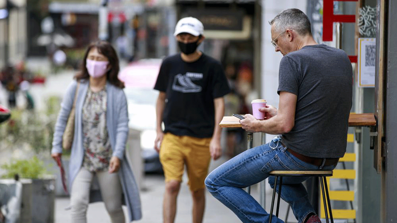 A man sits outside a cafe in central Auckland, New Zealand, Friday, December 3, 2021. Bars, restaurants and gyms reopened in Auckland on Friday as the last major parts of a 100-day lockdown ended.  New Zealand has begun a new phase in its virus response in which there will be no lockdown but people will be required to show permits for vaccinations for many services.  (Alex Burton/NZ Herald via AP)