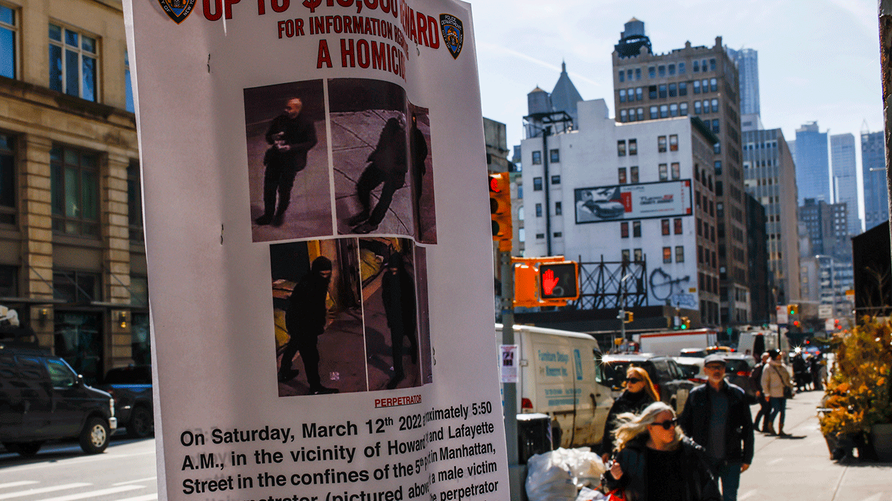 People walk by a bulletin posted by NYPD near the place where a homeless person was killed days earlier in lower Manhattan, Monday, March 14, 2022, in New York. A search is underway for a gunman who has been stalking and shooting homeless men sleeping on the streets of Washington, D.C., and New York City. Authorities say the gunman killed two people and wounded three more in less than two weeks. (AP Photo/Eduardo Munoz Alvarez)