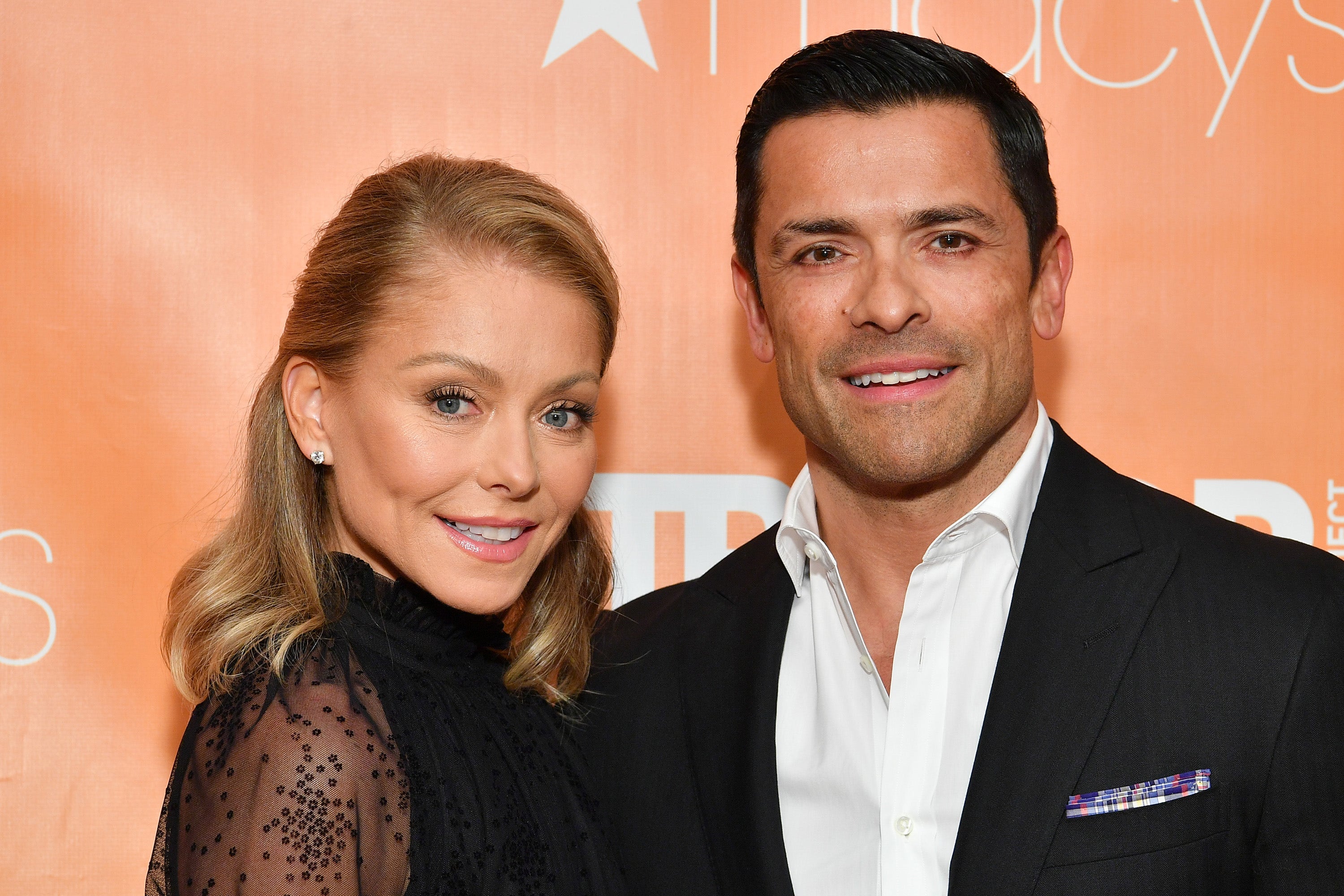 Kelly Ripa smiles in a black dress next to her husband Mark Consuelos in a white button down and black suit