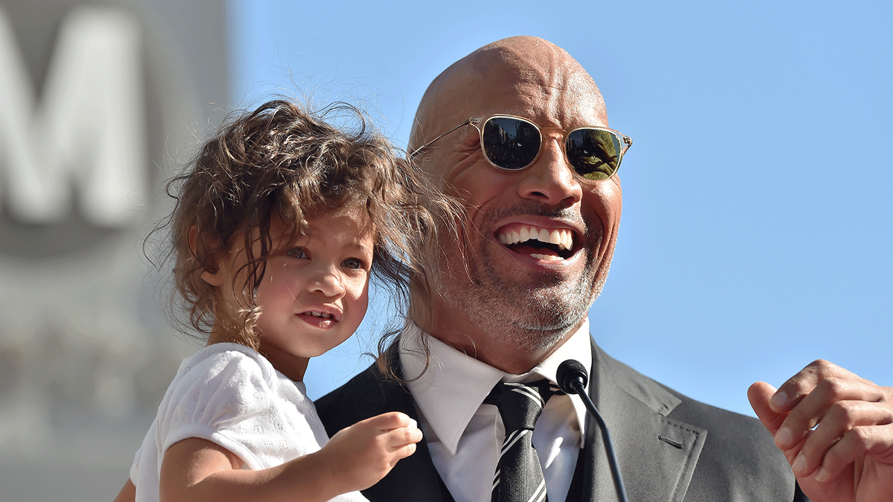 Dwayne Johnson holds his two kids while listening to wife Lauren