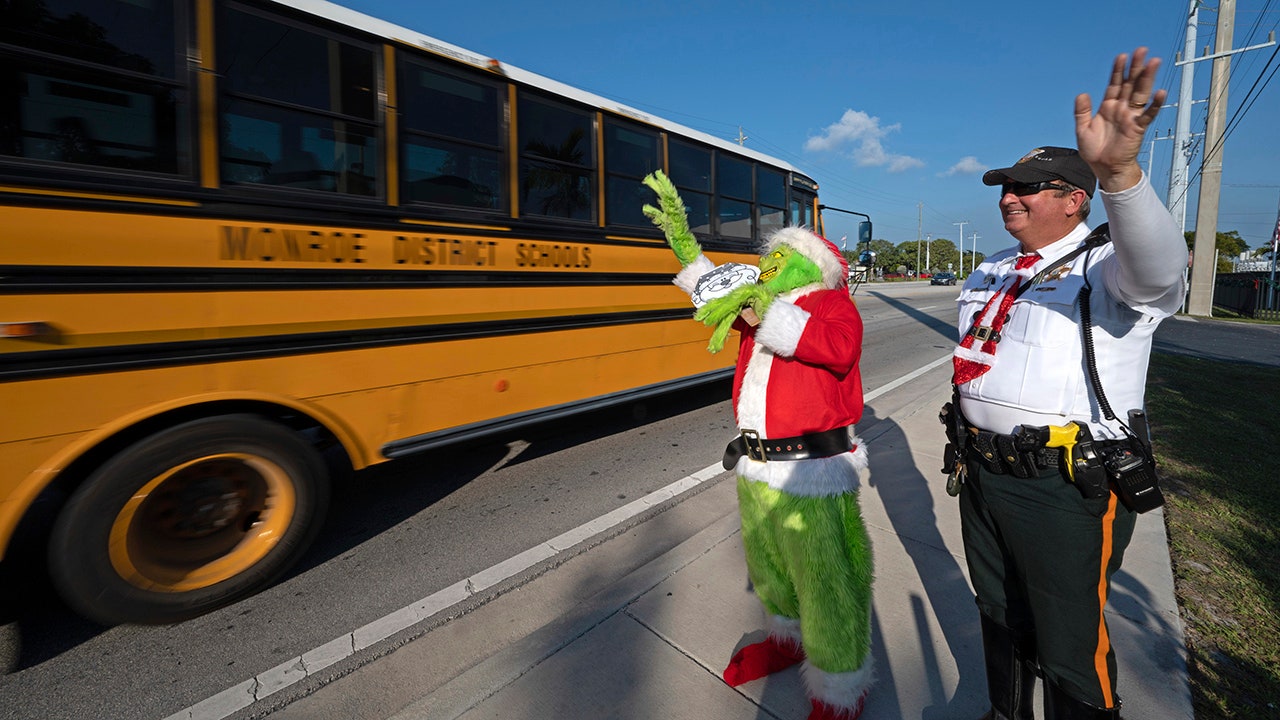In this photo provided by the Florida Keys News Bureau, Monroe County Sheriff's Office Colonel Lou Caputo, left, costumed as the Grinch, and Deputy Andrew Leird, right, wave at a school bus rolling on the Florida Keys Overseas Highway Tuesday, Dec. 13, 2022, in Marathon, Fla. When drivers are pulled over for slightly speeding through a school zone, Caputo offers them the choice between an onion or a traffic citation. It's a holiday tradition in the Keys that Caputo began 20 years ago. (Andy Newman/Florida Keys News Bureau via AP))