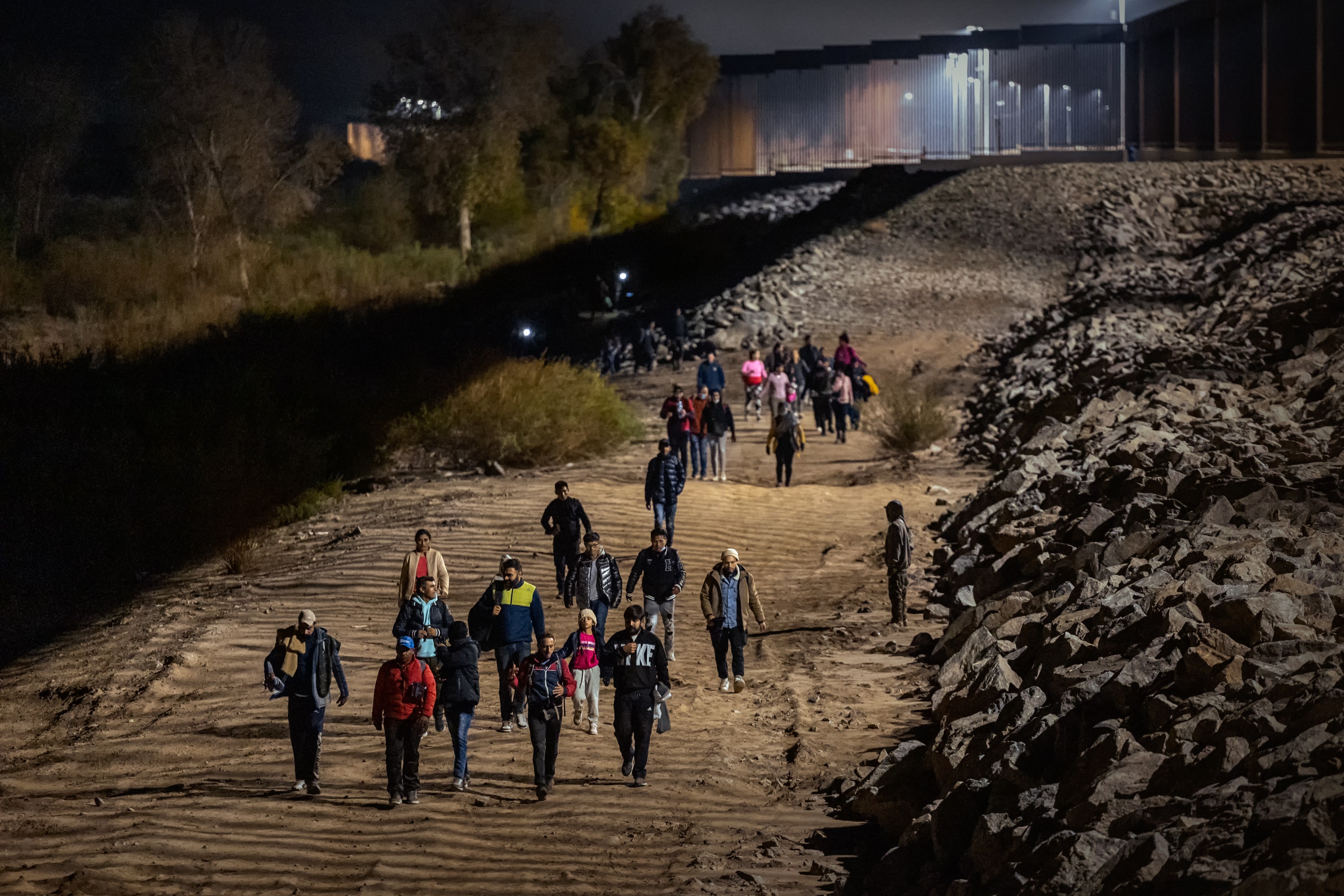 YUMA, ARIZONA - DECEMBER 30: Immigrants walk along the U.S.-Mexico border barrier on their way to await processing by the U.S. Border Patrol after crossing from Mexico on December 30, 2022 in Yuma, Arizona. (Photo by Qian Weizhong/VCG via Getty Images)