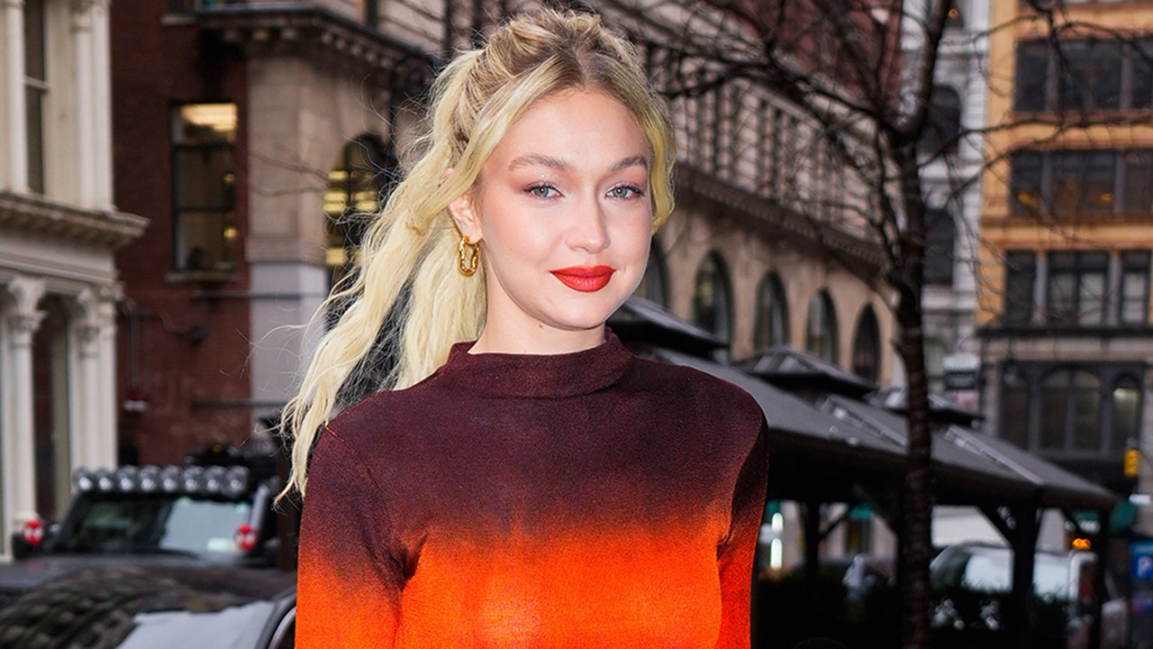 Gigi Hadid smiles at the camera while walking in New York City in an ombré maroon and red dress
