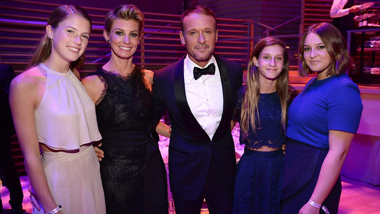 Maggie McGraw in a blush halter top and skirt smiles next to mother Faith Hill in a long black dress, husband Tim McGraw in a classic black tuxedo, daughter Audrey in a blue dress, and daughter Gracie in a blue dress