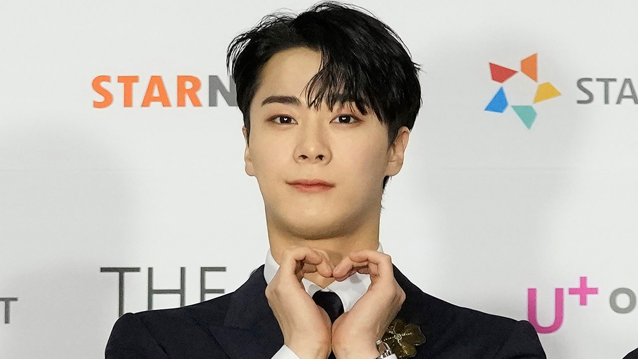 Moon Lim on the red carpet making a heart with both his hands and soft smiling for the camera