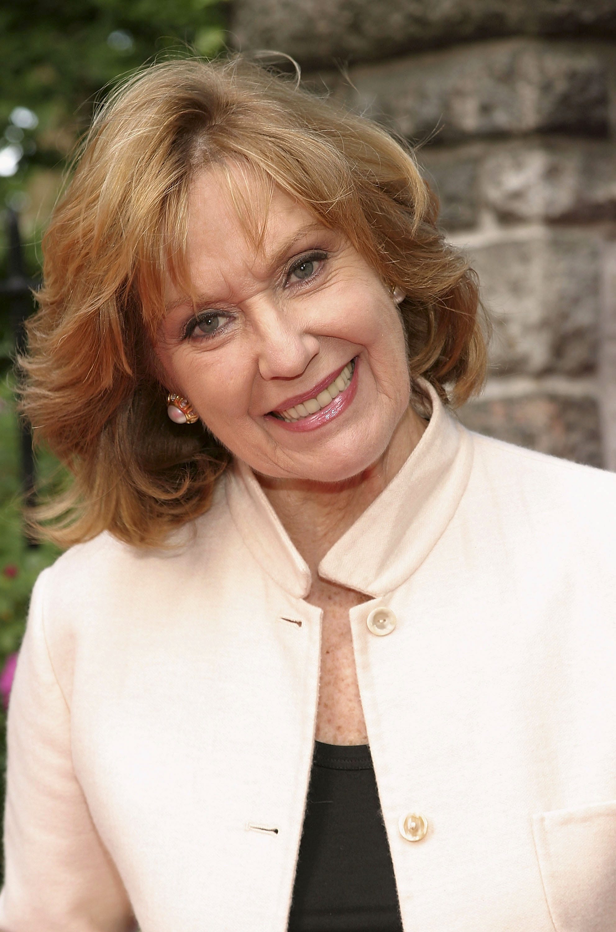 Elizabeth Hubbard smiling with head tilted in cream jacket