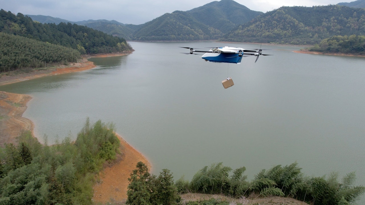 Photo of a drone carrying a box over a lake.