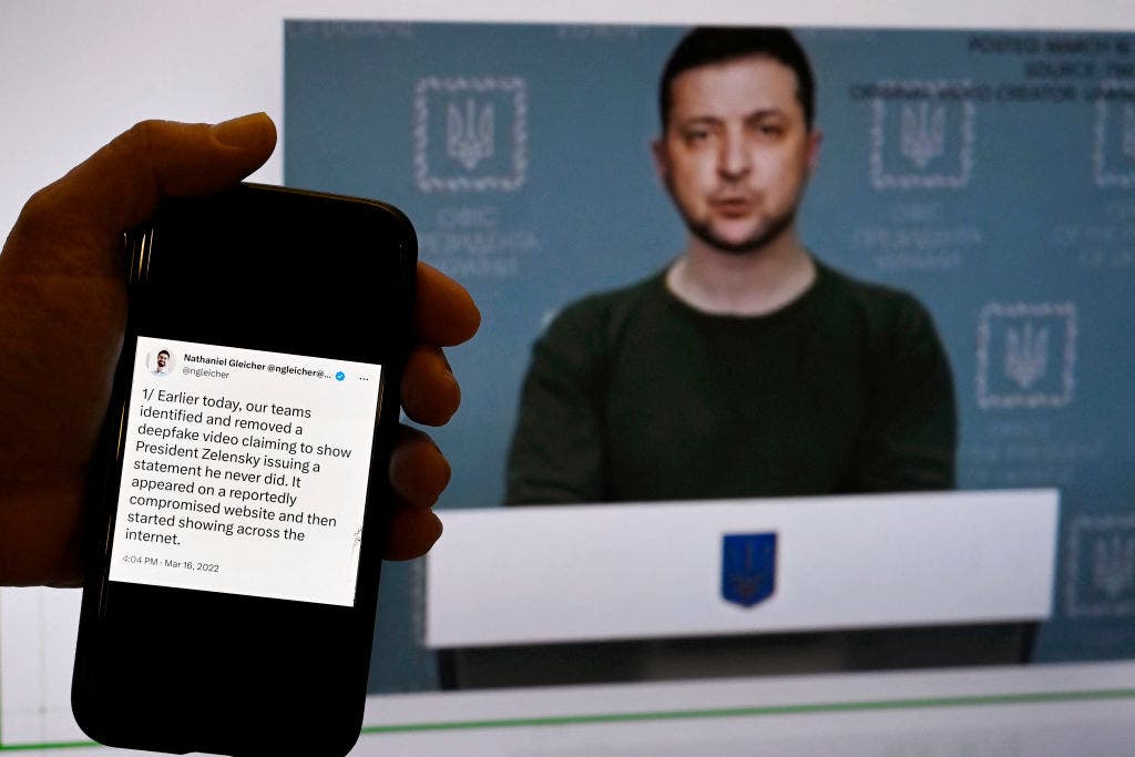 This illustration photo taken on January 30, 2023 shows a phone screen displaying a statement from the head of security policy at META with a fake video of Ukrainian President Volodymyr Zelensky calling on his soldiers to lay down their weapons shown in the background, in Washington, D.C. (OLIVIER DOULIERY/AFP via Getty Images)