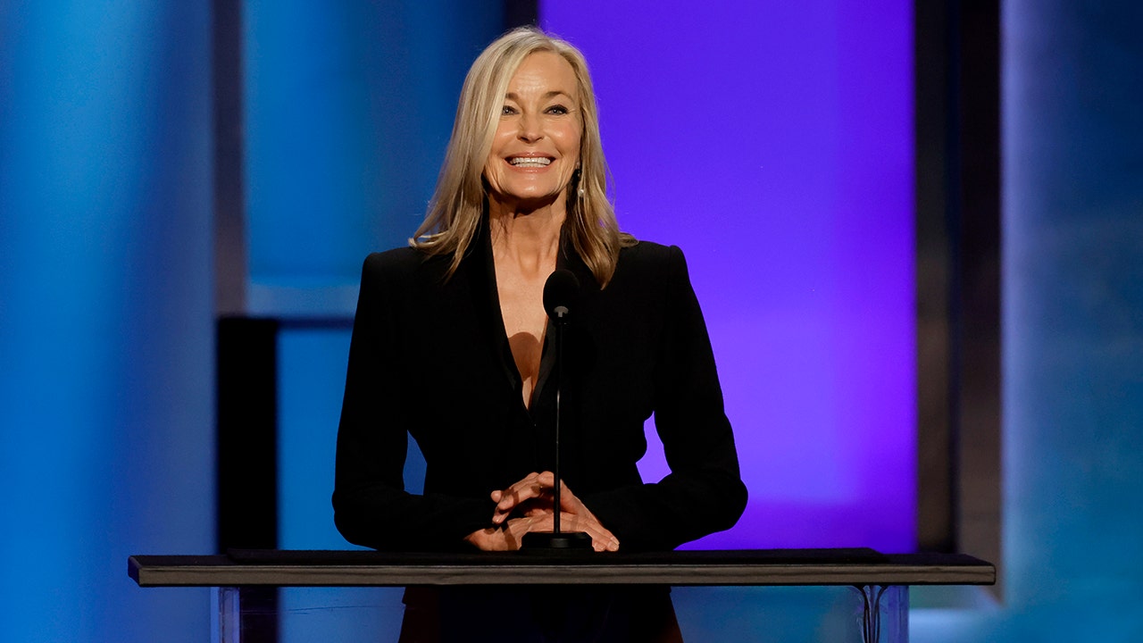 Bo Derek wearing black and smiling while standing in front of a podium