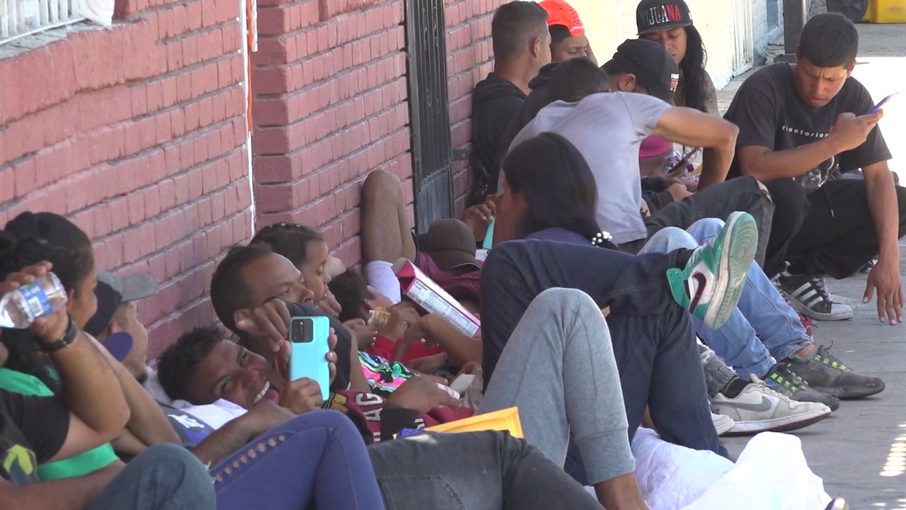 A row of migrants lay against a brick wall waiting