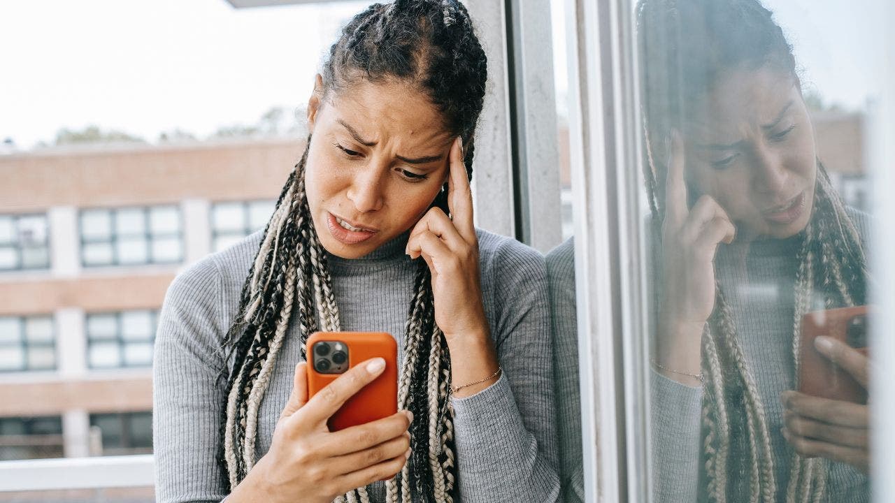 Stressed woman with hand on head, looking down at iPhone