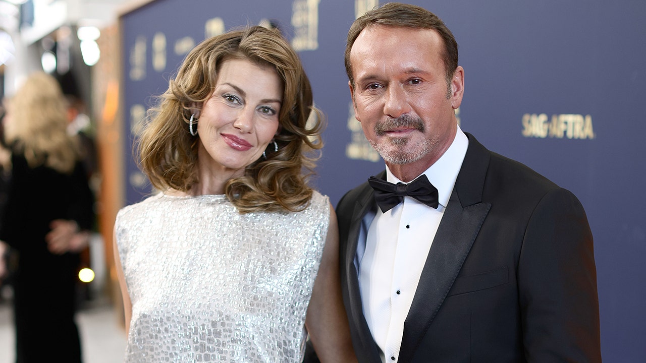 Faith Hill soft smiles in a white dress next to Tim McGraw in a classic tuxedo also soft-smiling at the SAG Awards