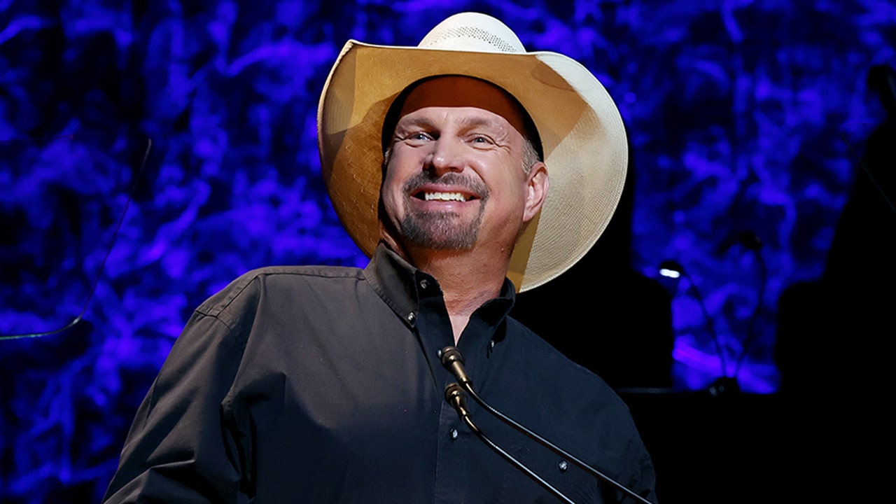 Garth Brooks smiles in a tan cowboy hat and black shirt onstage at the County Music Hall of Fame and Museum