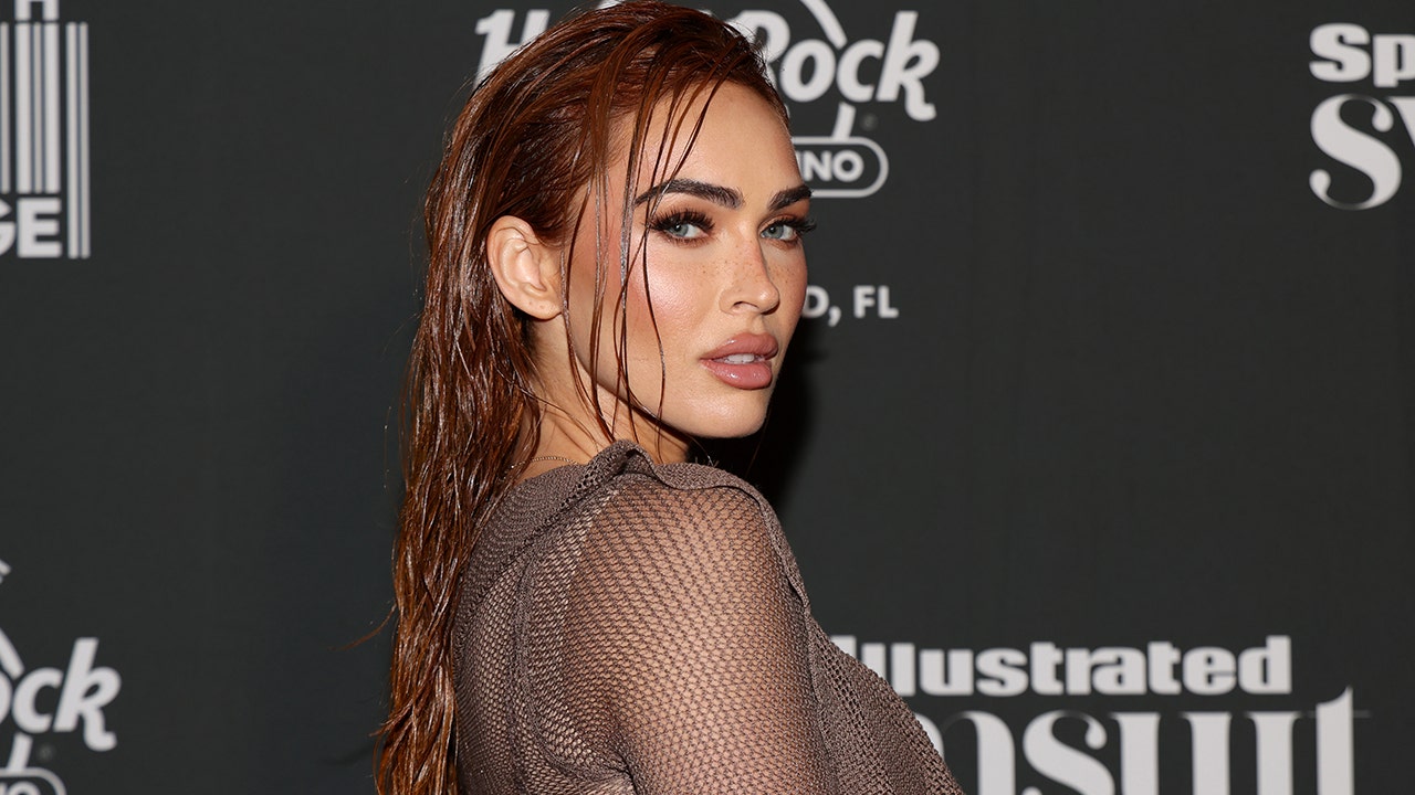 Megan Fox in a mesh dress looks back at the camera with wet hair for a Sports Illustrated Swimsuit event