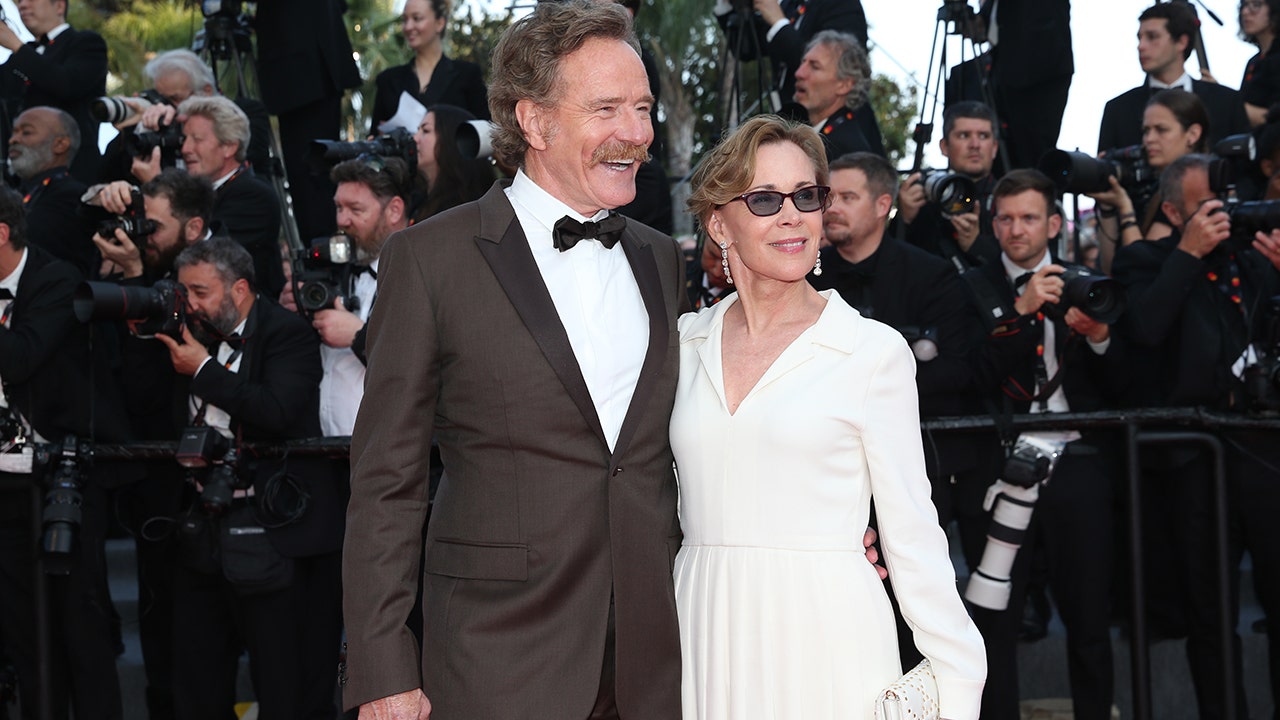 Bryan Cranston wearing a suit and bowtie on the red carpet with his wife Robin wearing a white dress