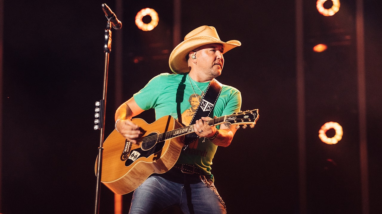 Jason Aldean wears a green T-shirt and holds his guitar on stage at CMAFest