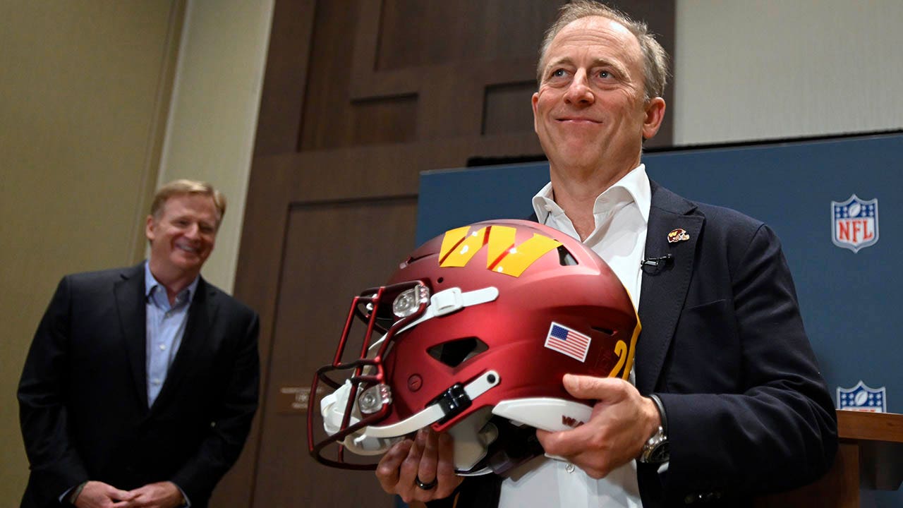 Josh Harris holds a Commanders helmet