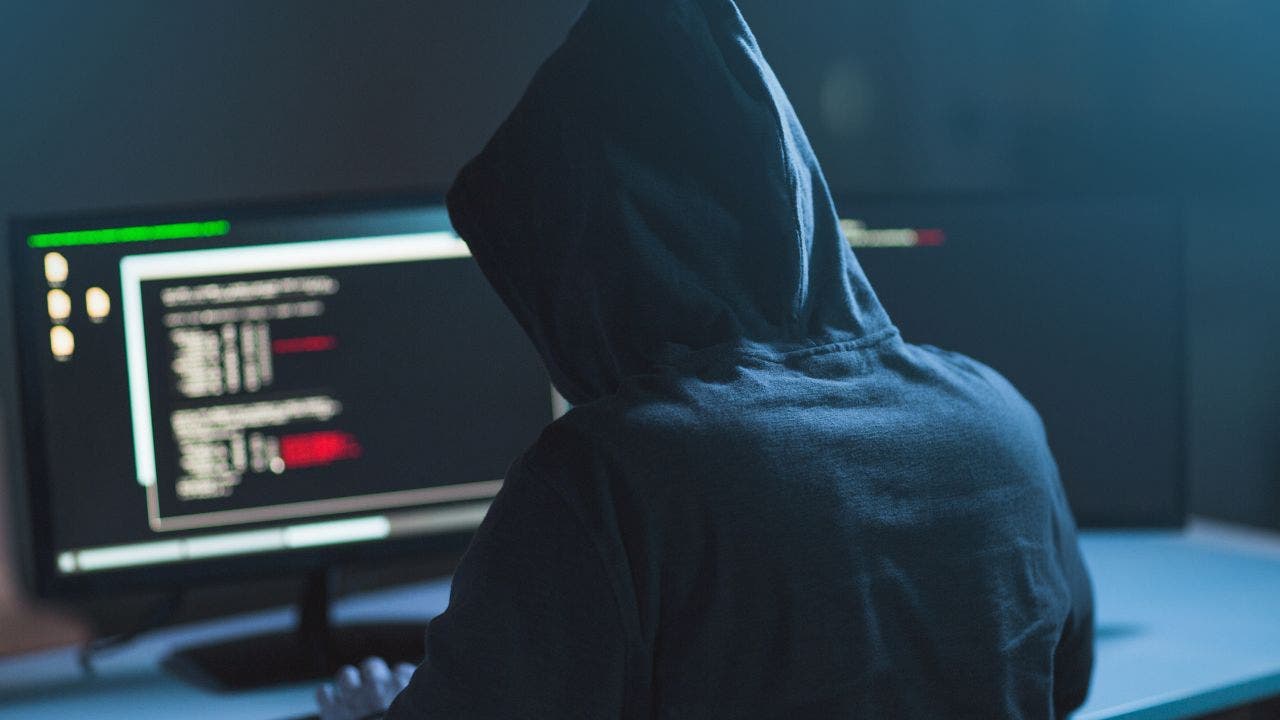 The back of a cybercriminal in hoodie hacking a laptop