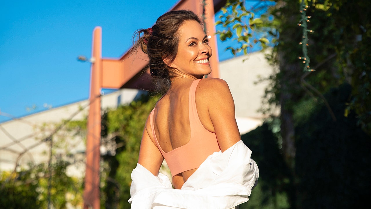 Brooke Burke wearing a peach tank top while looking behind with a white blouse