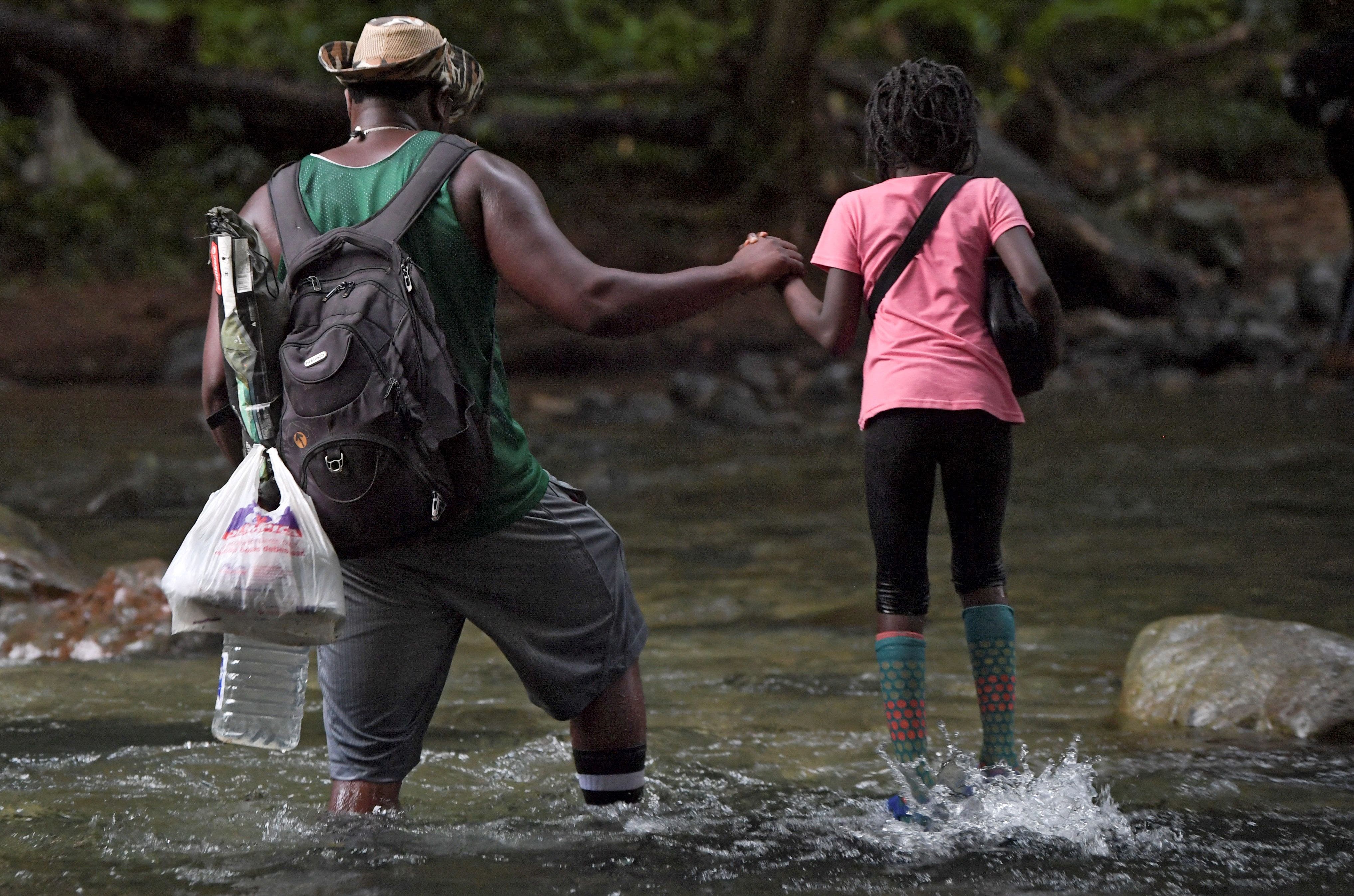 Un migrante haitiano sostiene la mano de una niña mientras cruzan la jungla del Tapón del Darién, cerca de Acandí, departamento de Chocó, Colombia, en dirección a Panamá, el 26 de septiembre de 2021, en su camino tratando de llegar a los EE. UU.