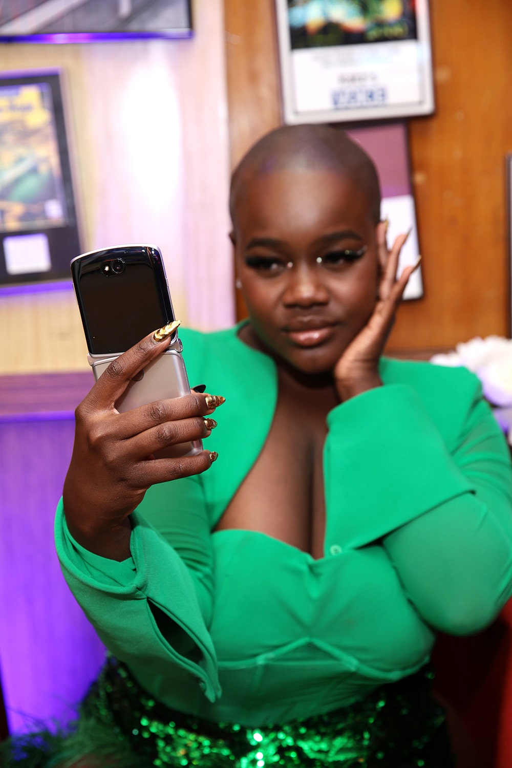 Achieng Agato is wearing a bright green top and holding a cell phone.