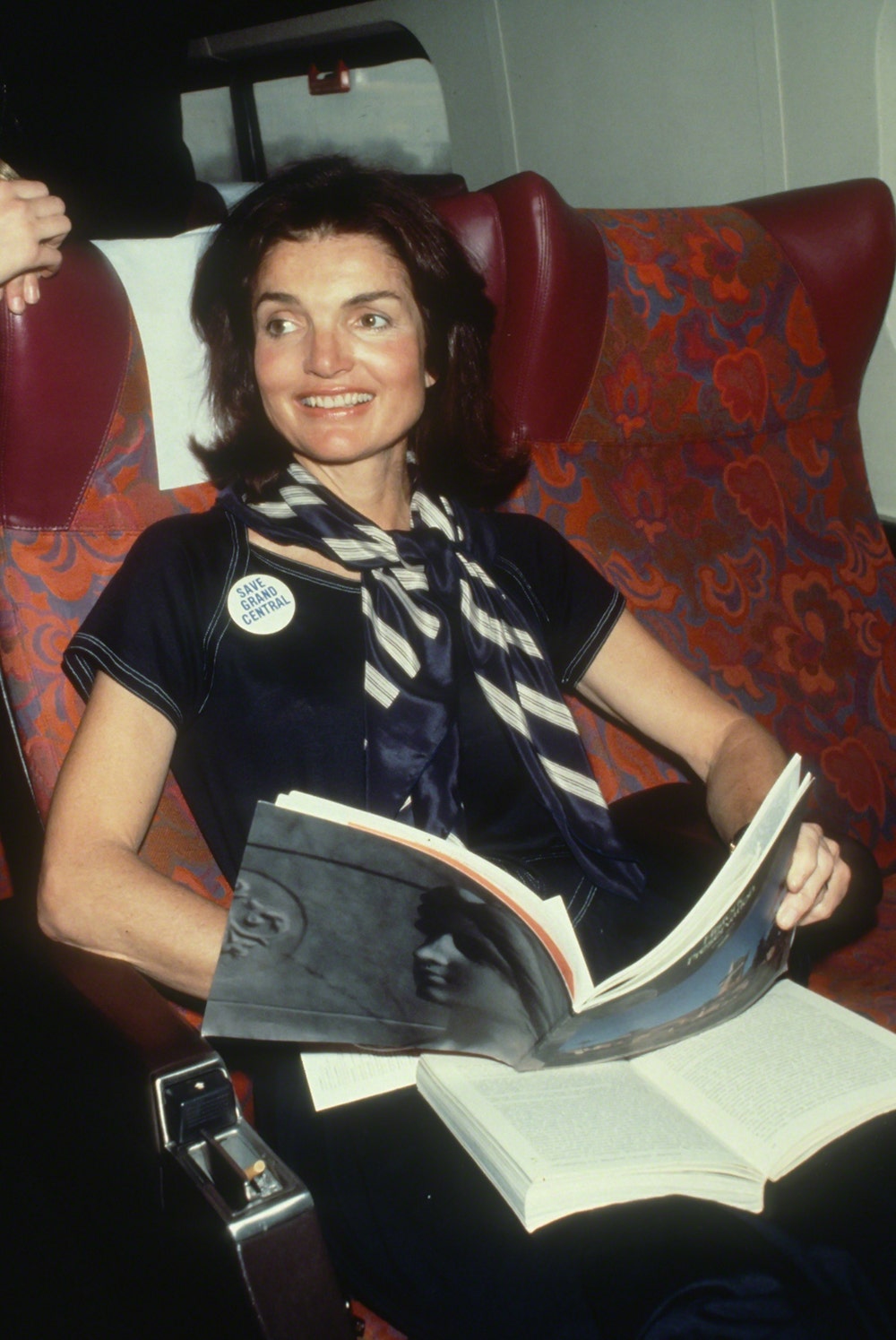 Jackie Kennedy wearing a navy suit holding a book