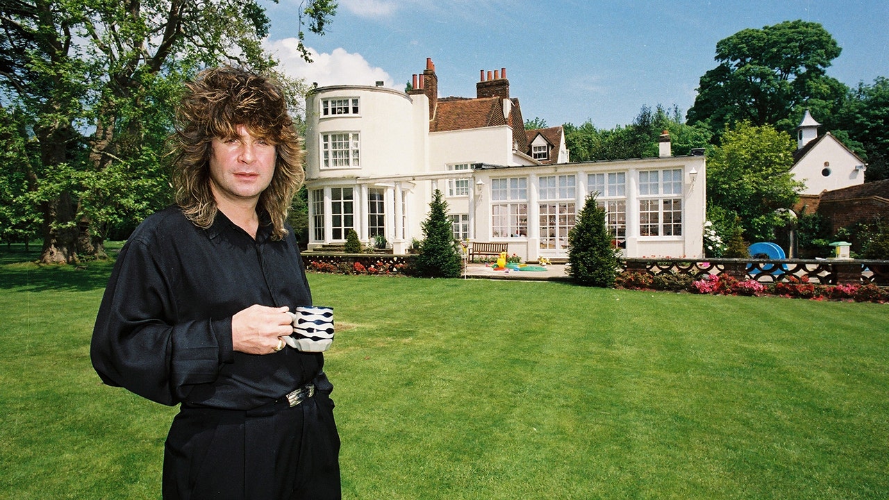 Black Sabbath singer Ozzy Osbourne holding a cup of tea in the garden of his home while wearing a black robe