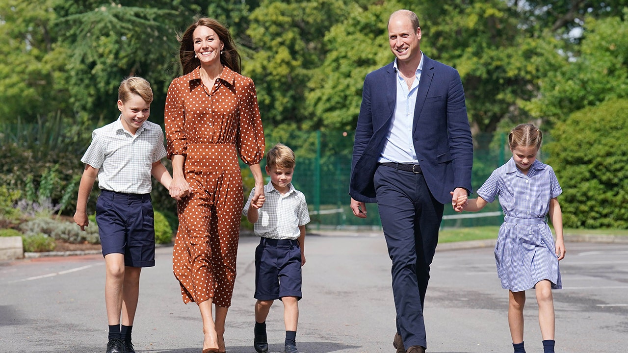 Kate Middleton wearing a brown and white polka dot dress walking alongside prince william in navy slacks and a blazer with their three children