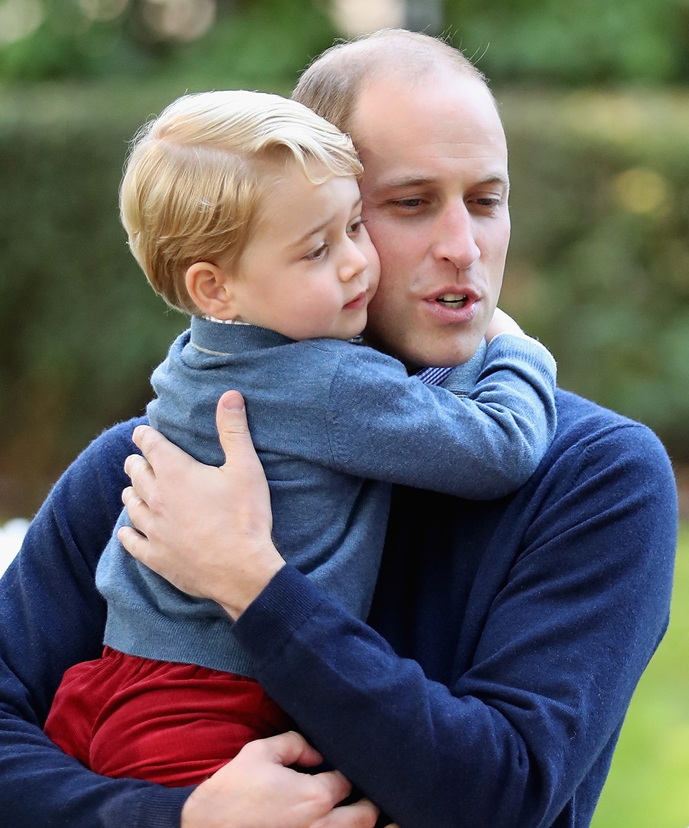 Prince William wearing a blue sweater holding Prince George wearing a matching blue sweater