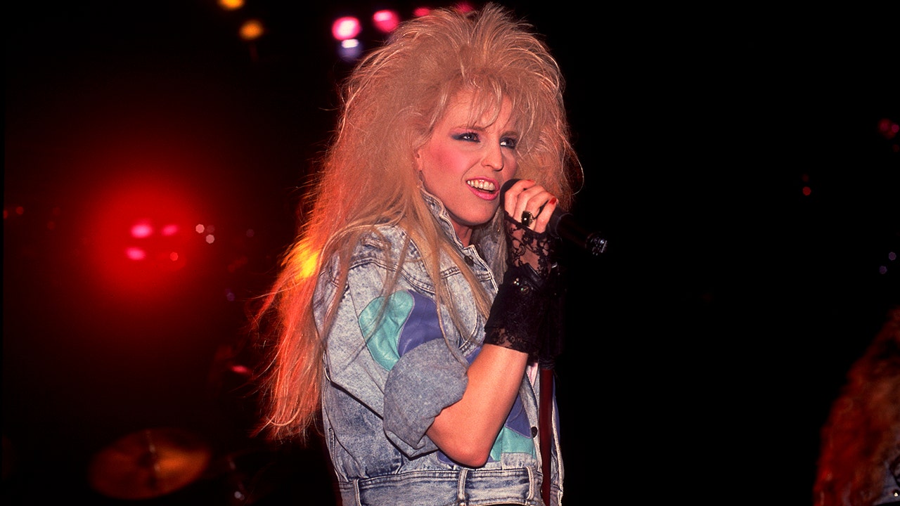 Janet Gardner wearing a denim jacket holding a mic