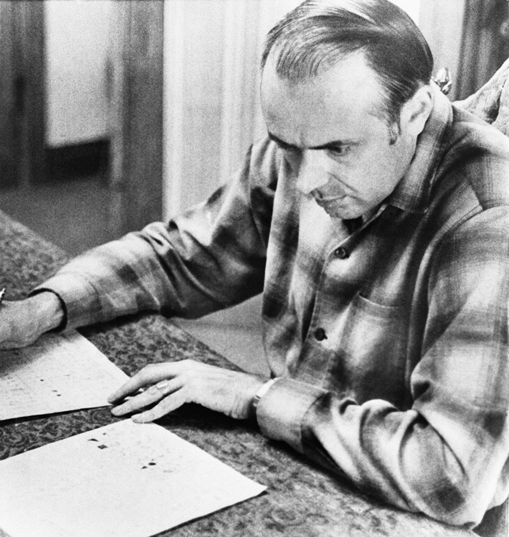Donald G. Harden wearing a plaid shirt and looking at a stack of papers