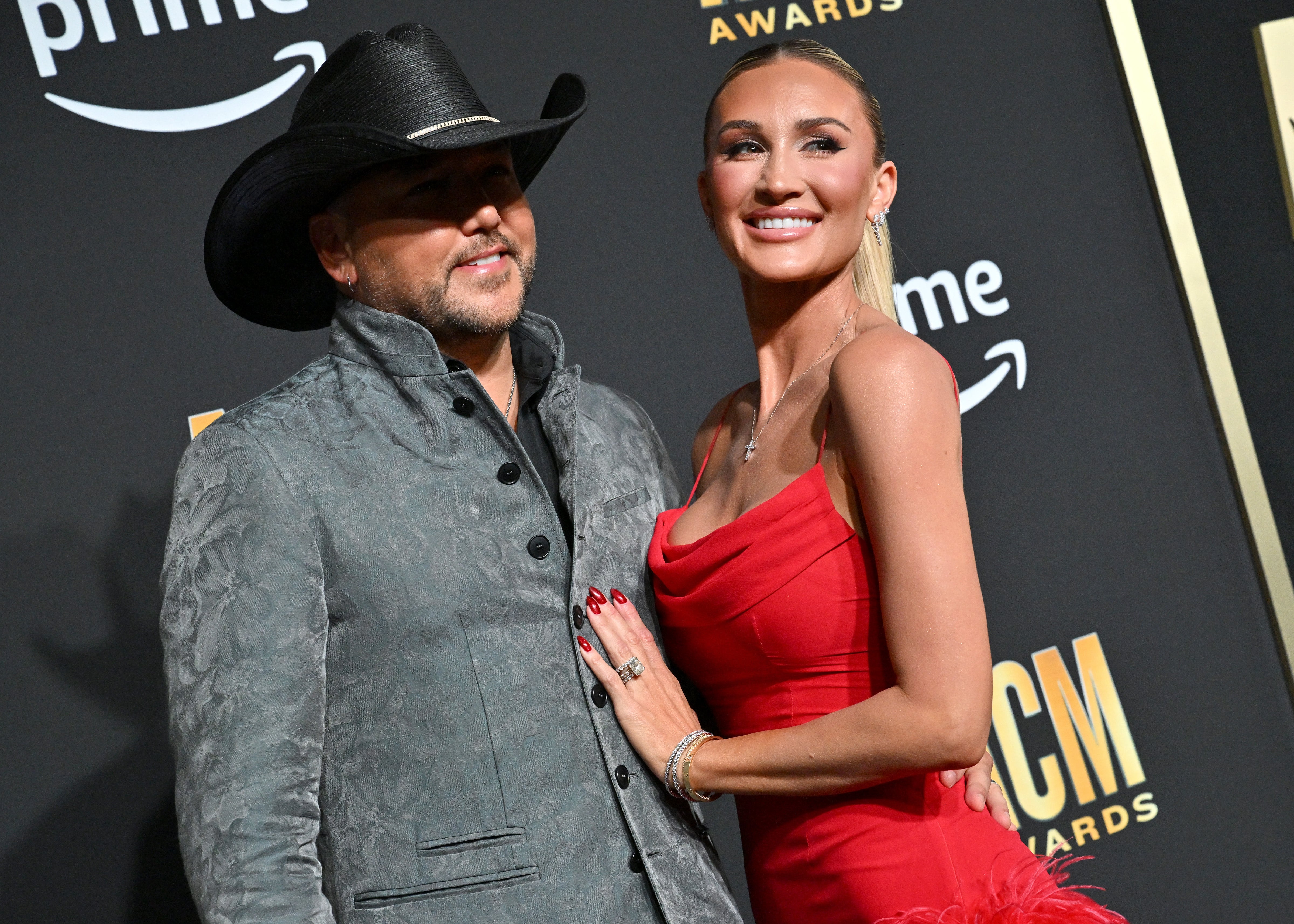 Jason Aldean in a suit and cowboy hat with Brittany Aldean in a red dress