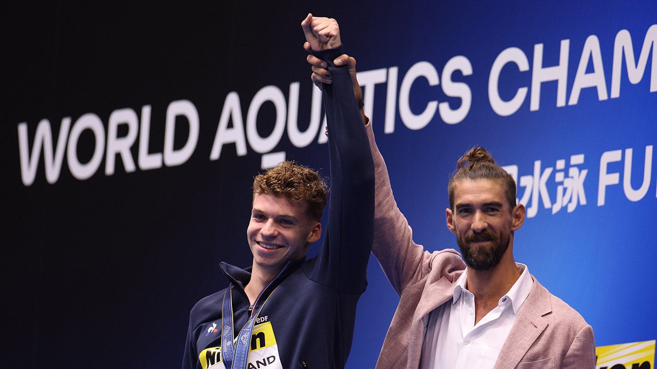 Michael Phelps raises Leon Marchand's arm