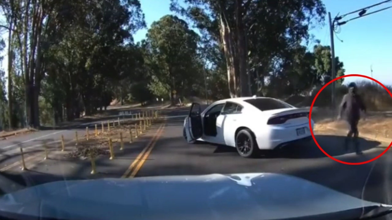 A second suspect wearing a black ski mask gets out of the passenger side of the Charger