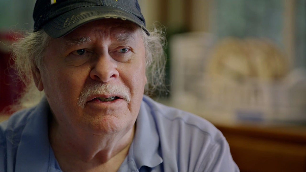 An older man wearing a light blue shirt and a cap