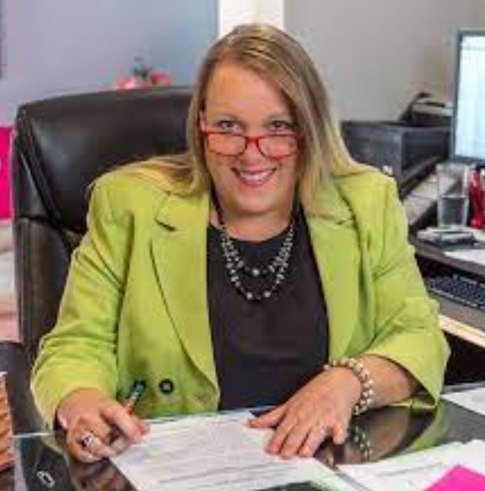 Woman in neon green blazer and red-rimmed reading glasses.