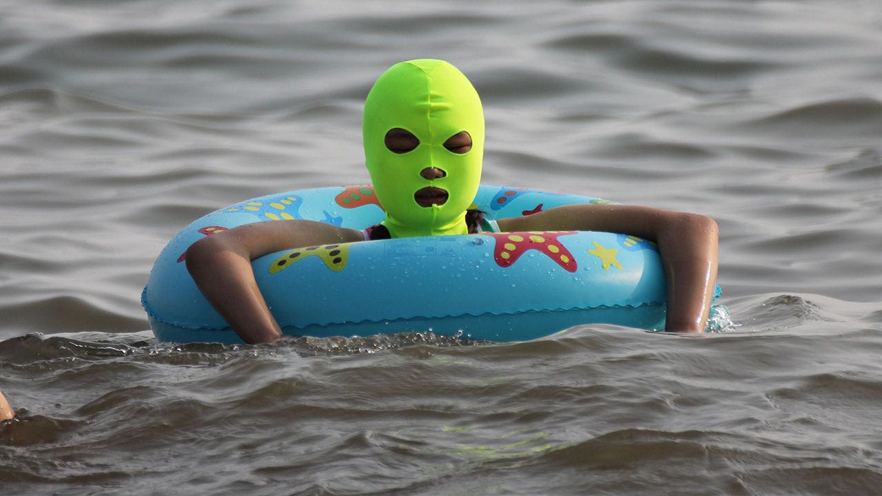 Frau trägt grünen Facekini, während sie im Wasser watet