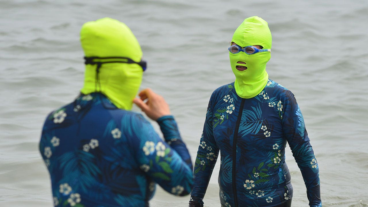 Two women wear matching swimsuits and green facekinis