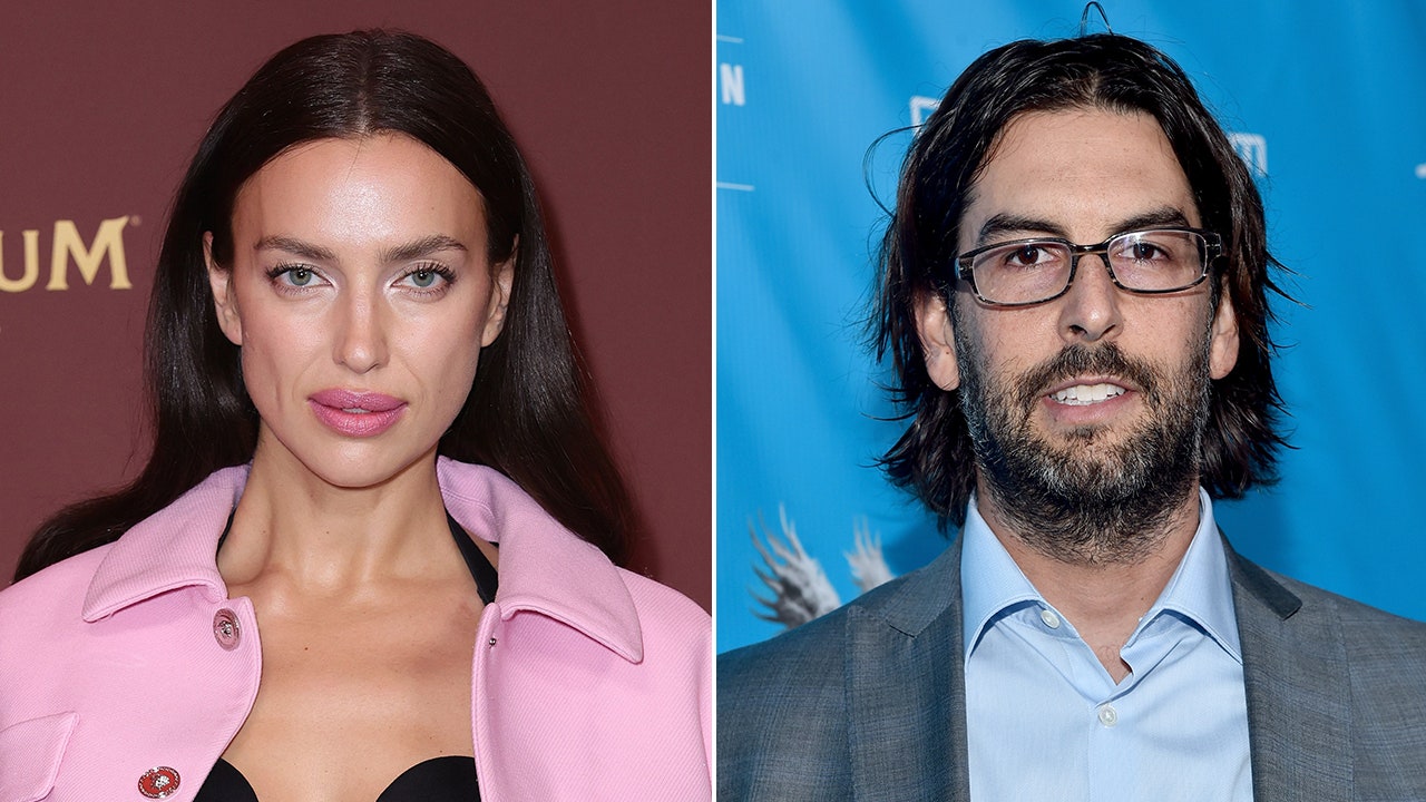 Irina Shayk looks at the camera on the carpet in a bubblegum pink jacket split Rob Bourdon smiles at the camera in a light blue shirt and grey suit