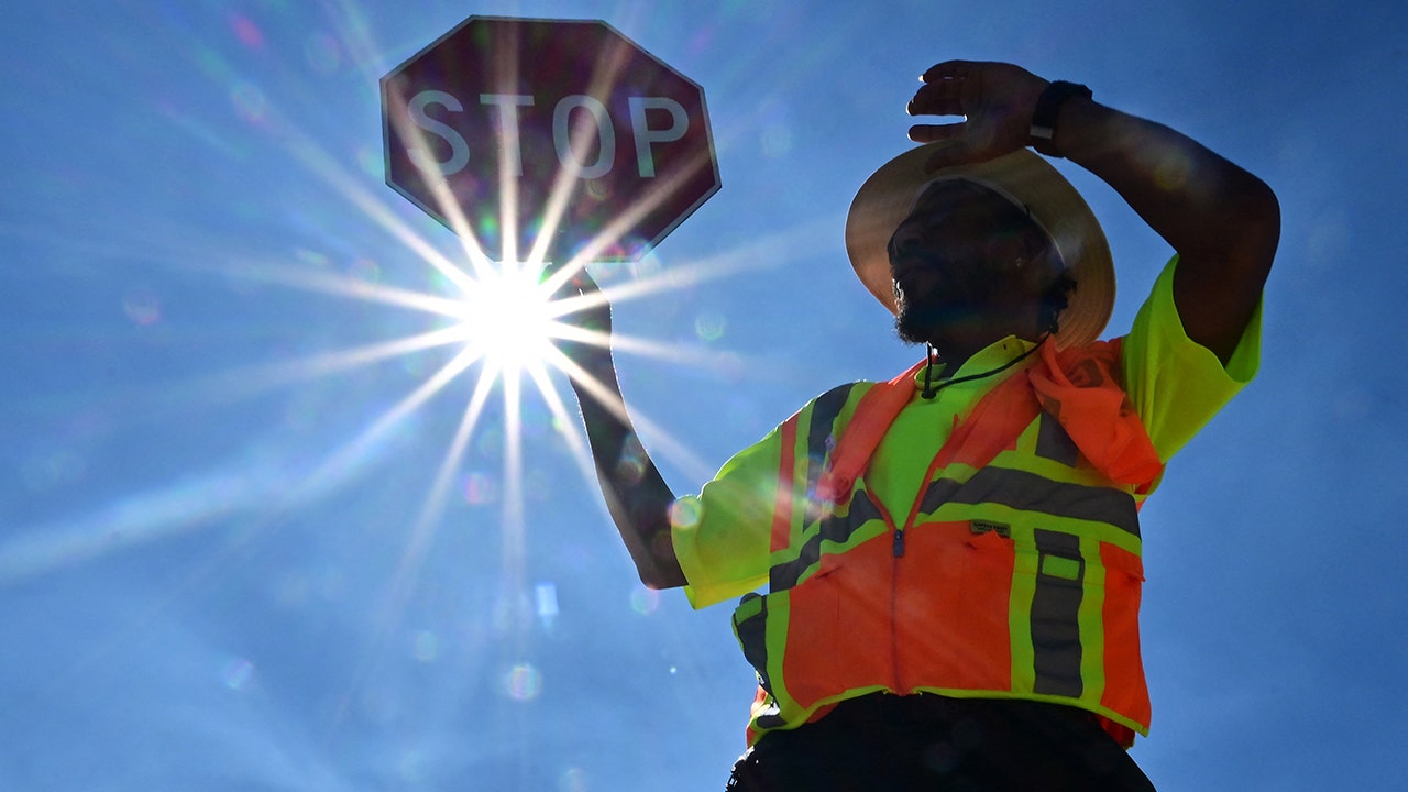 A traffic warden holds a stop sigh as the sun beats down on him